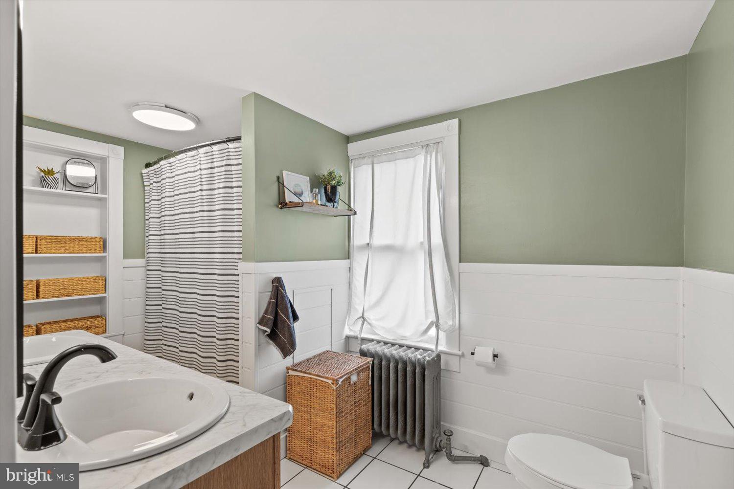 Bathroom with sage-green walls, white paneling, a marble-look vanity, and a striped shower curtain.