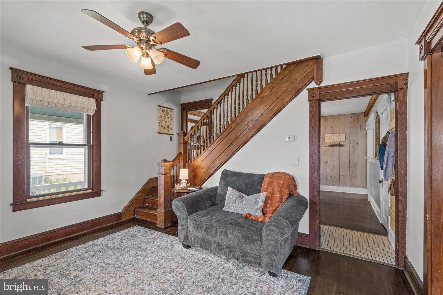 Living room with a dark wood staircase, gray armchair, patterned rug, and ceiling fan.