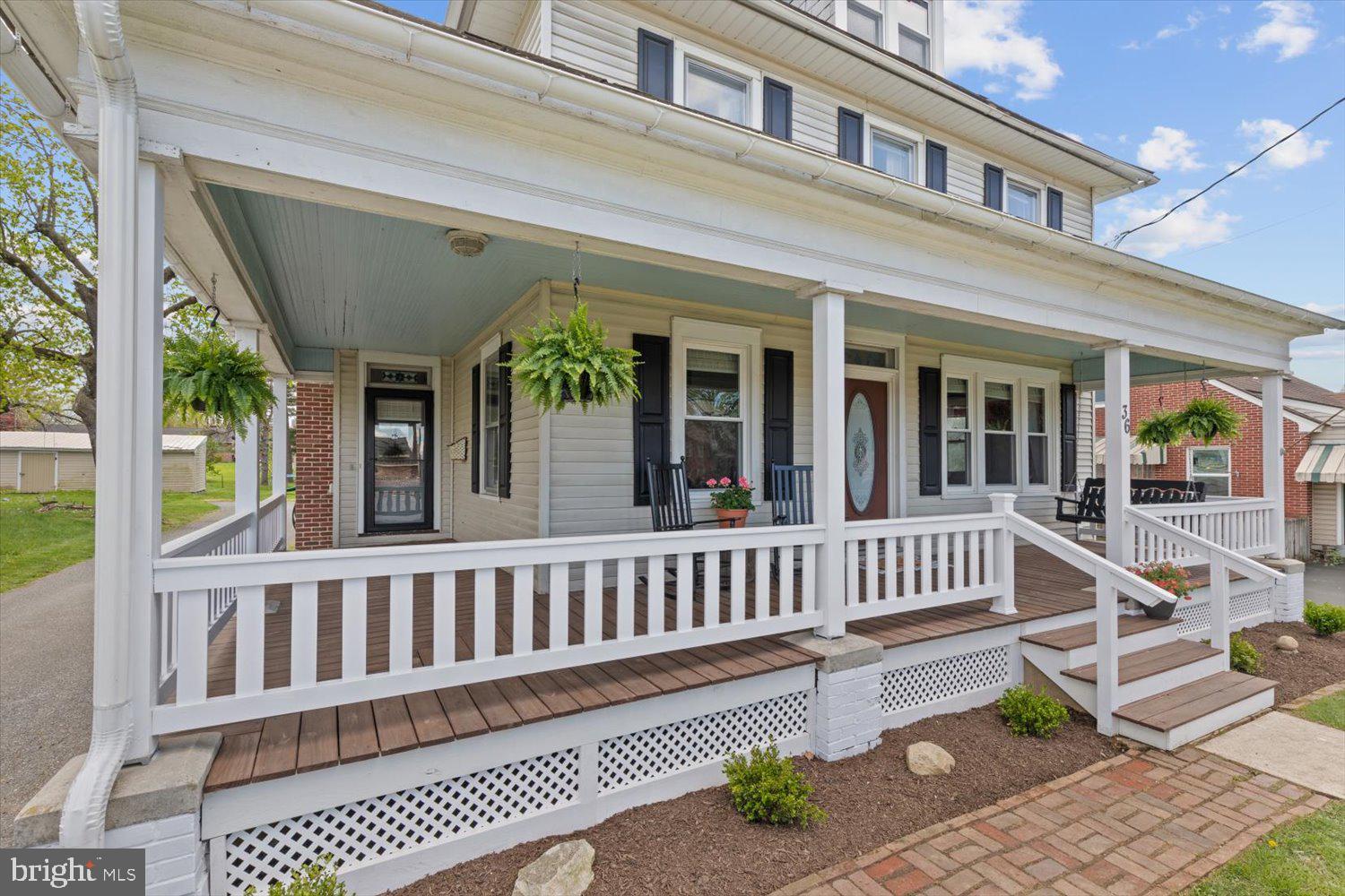 Two-story home with a broad covered porch, white railings, hanging ferns, and dark shutters.