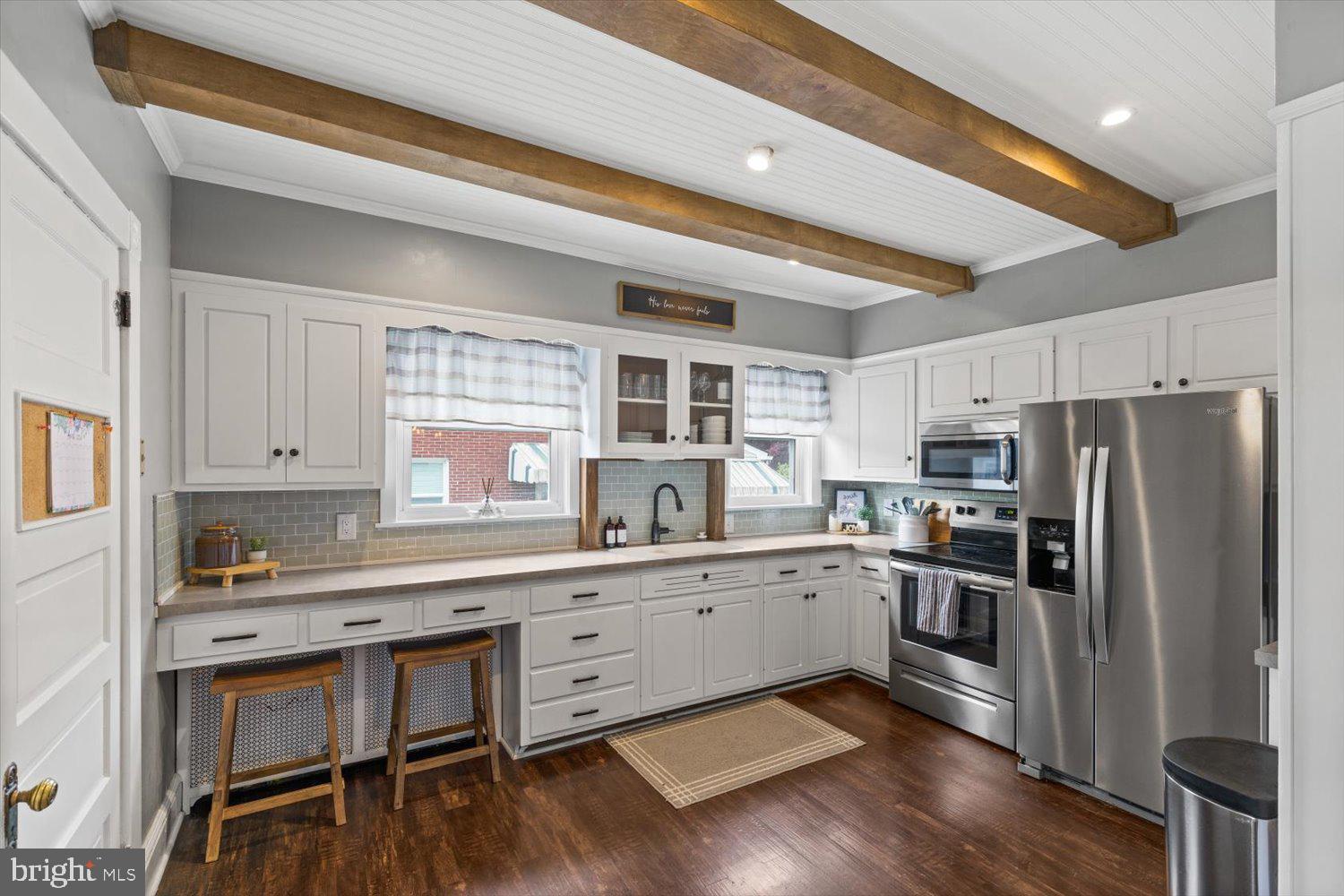 Kitchen with white cabinetry, stainless steel appliances, gray tile backsplash, and exposed wooden ceiling beams.