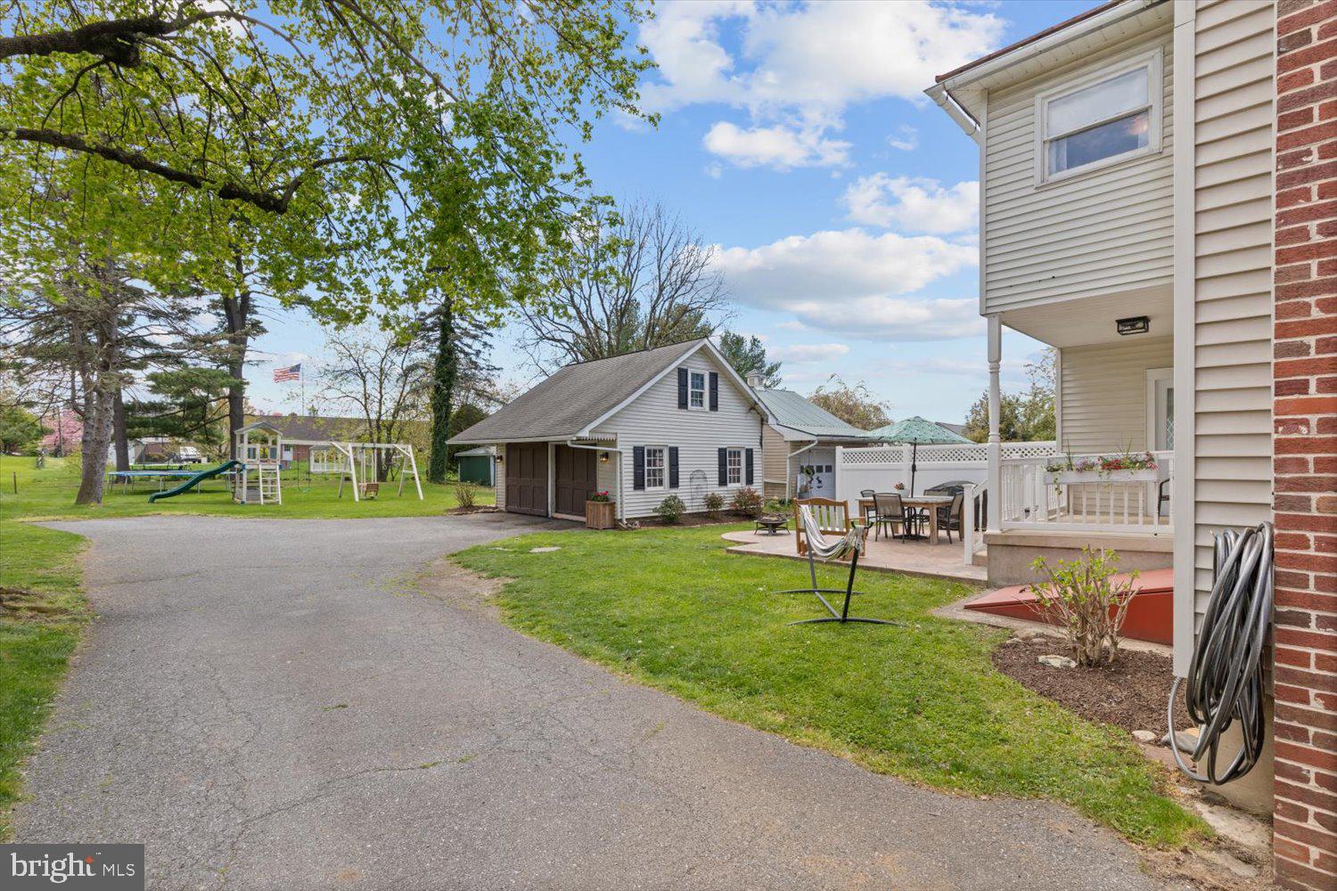 Home’s side yard with detached garage, paved driveway, playset, and patio seating.