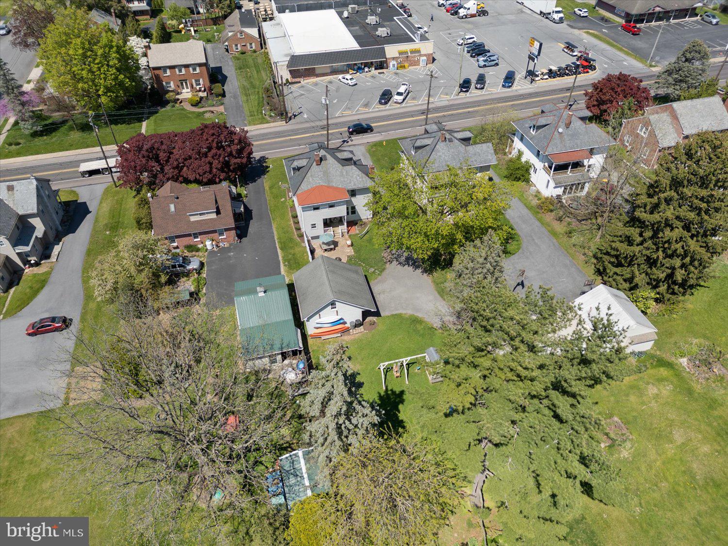 Aerial view of the property’s large lawn, neighboring homes, and shopping center across the road.