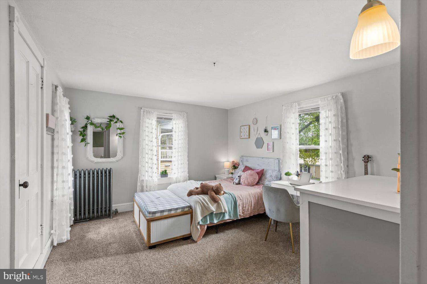 Bedroom with pink and teal bedding, two bright windows, and a built-in desk.