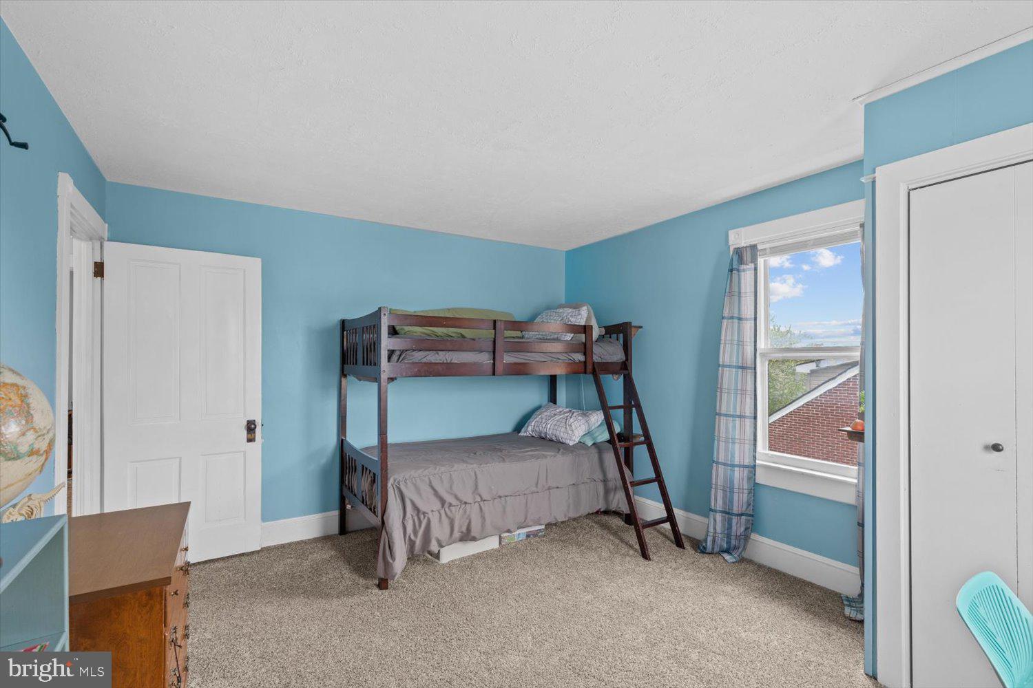 Bedroom with a dark wood bunk bed, blue walls, and a window overlooking a neighboring brick building.