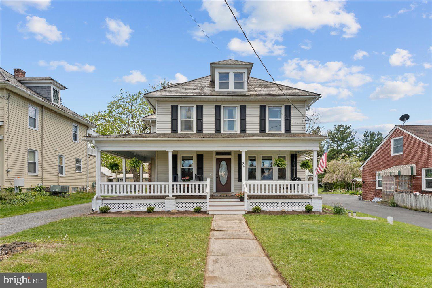 Two-story house with a covered wraparound porch, black shutters, and a central dormer.