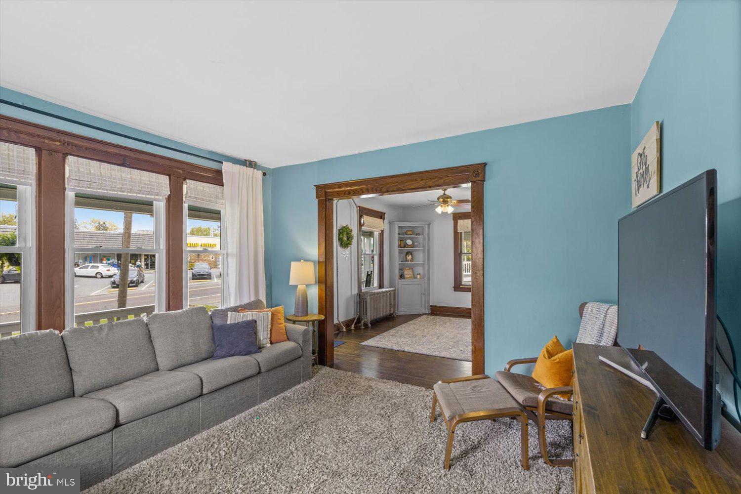 Living room with turquoise walls, a gray sofa, and large street-facing windows.