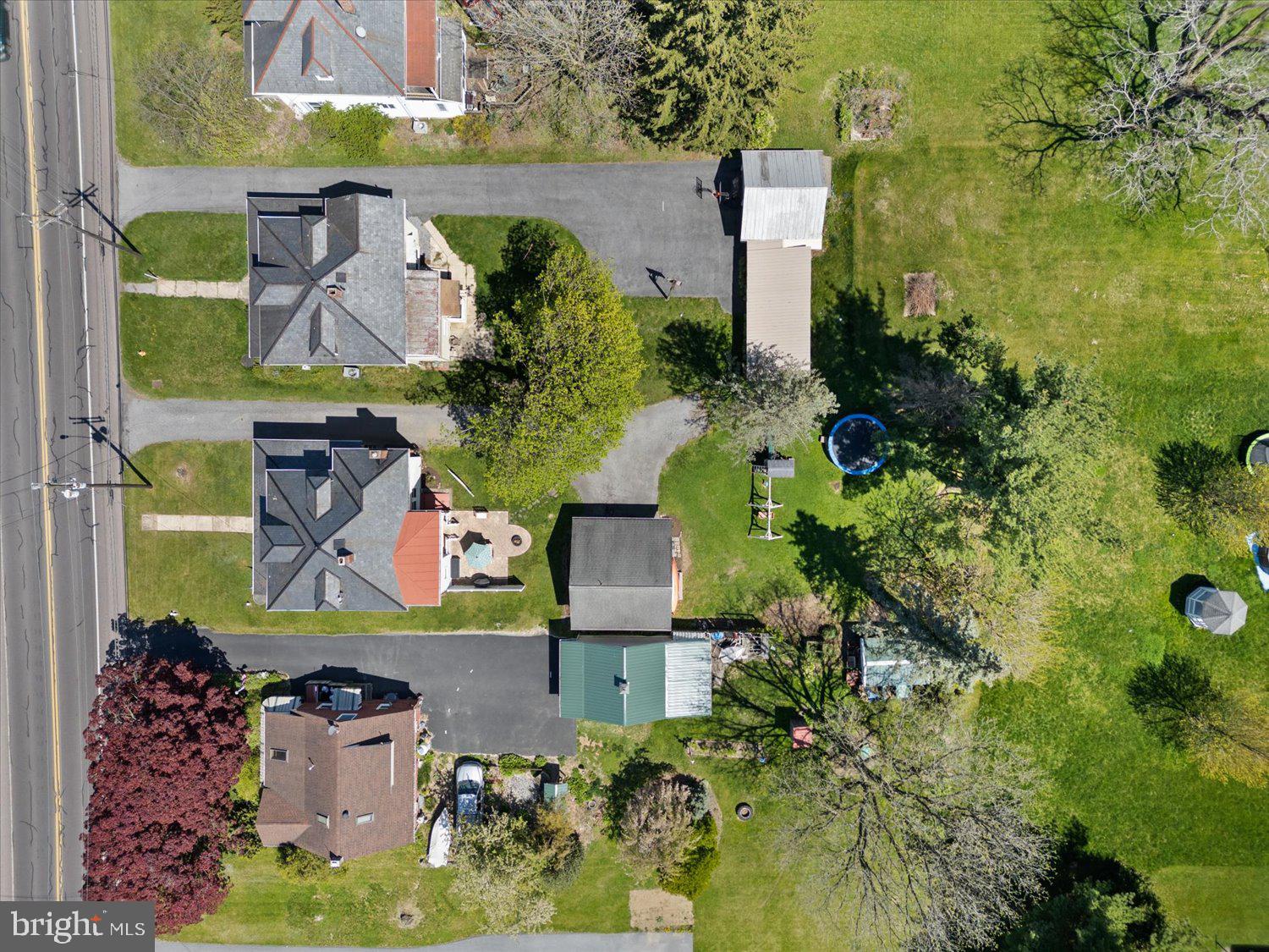 Aerial view of buildings and paved parking beside a road, surrounded by lawns and mature trees.