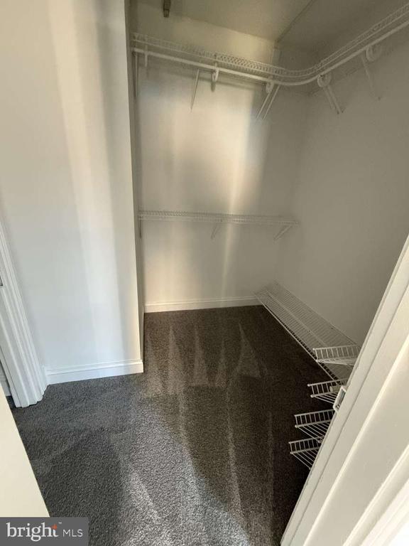 Empty walk-in closet with dark carpet and white wire shelving.