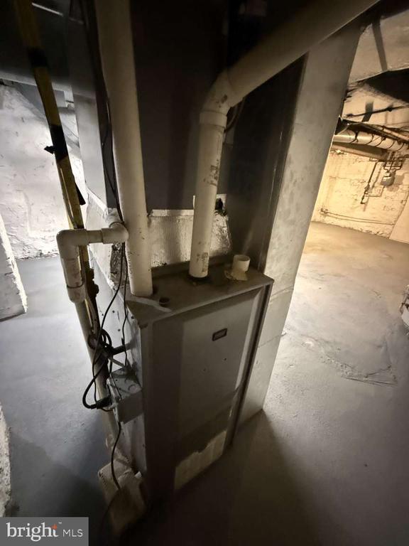 Basement furnace with exposed pipes and bare concrete floors.