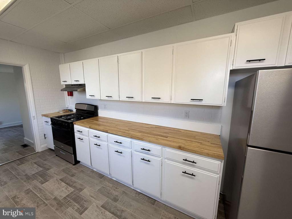 Kitchen with white cabinets, butcher-block countertops, and a black gas range.