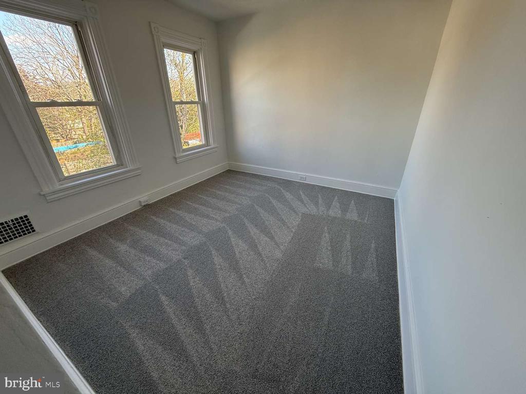 Empty bedroom with gray carpet and two windows along one wall.