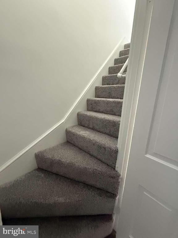 Carpeted staircase with gray steps, white walls, and a handrail.
