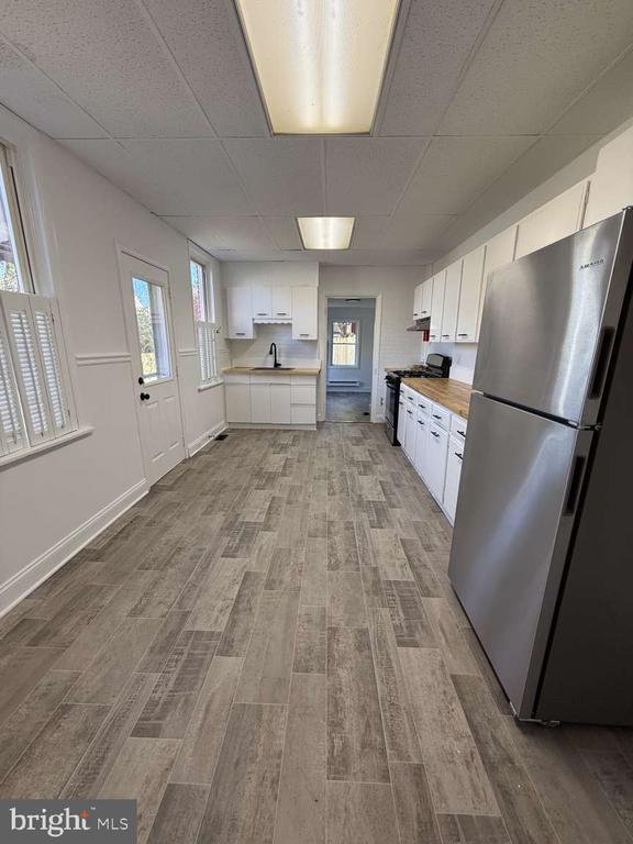 Kitchen with white cabinets, stainless steel refrigerator, and gray plank flooring.