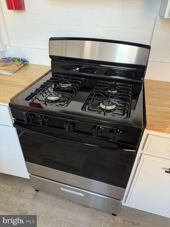 Kitchen gas range with four burners, stainless steel trim, and butcher-block countertops.