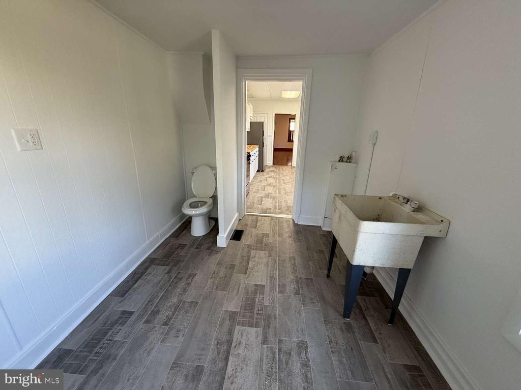 Utility room with a toilet, deep freestanding sink, and gray tile flooring.