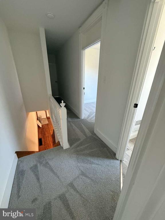 Upstairs hallway with gray carpeting, open doorways, and stairs leading down to a hardwood floor.