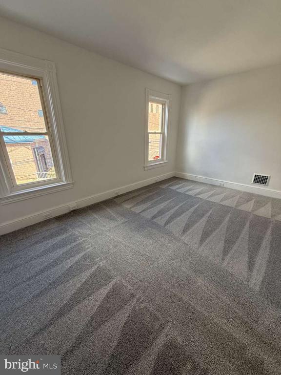 Empty room with gray patterned carpet and two windows.