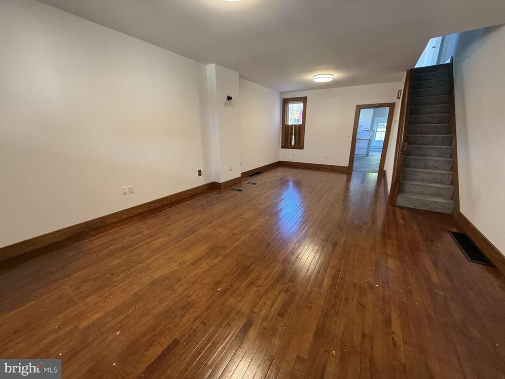 Vacant room with polished hardwood floors and a carpeted staircase.