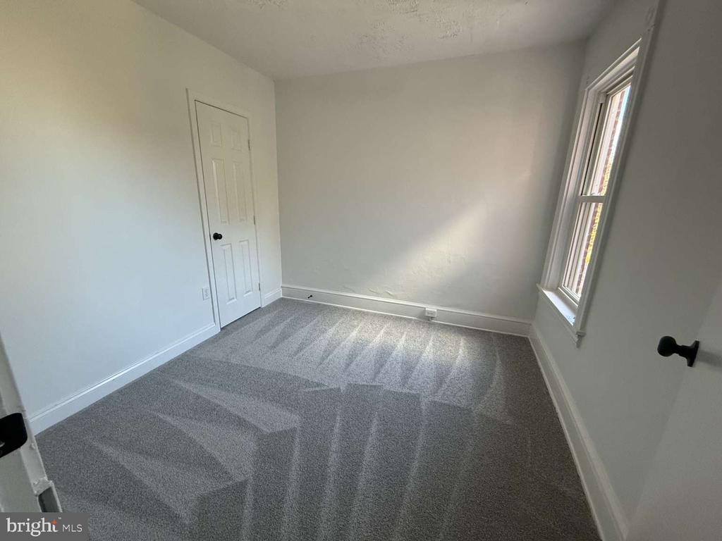 Empty bedroom with gray carpet and a tall sunlit window.
