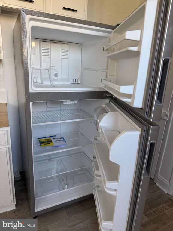 Open stainless-steel refrigerator with an upper freezer and empty shelves in a kitchen.