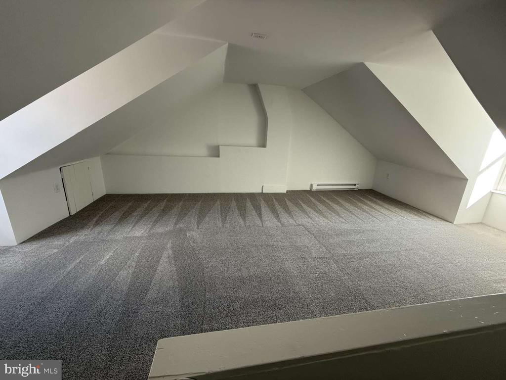 Vacant carpeted attic room with sharply sloped ceilings and a small access door.