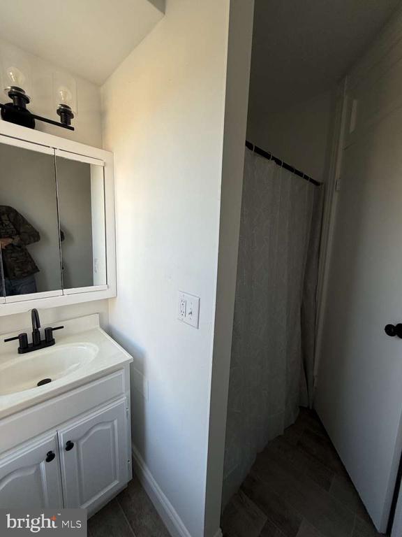 Bathroom with a white vanity and mirrored medicine cabinet beside a curtained shower.