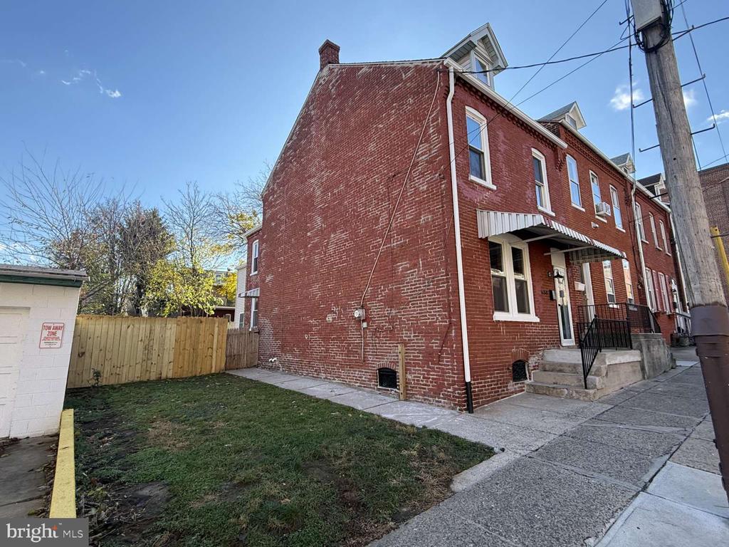 Red brick row house with a striped entrance awning, concrete steps, and a small fenced yard.