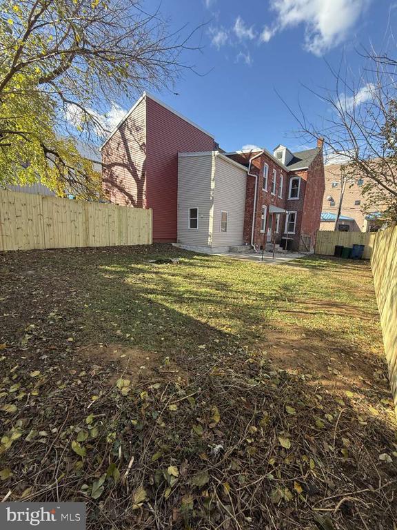 Home’s rear exterior beyond a fenced yard with fallen leaves and bare trees.