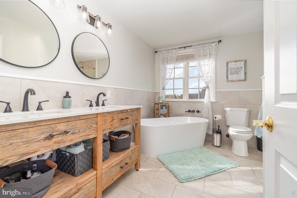 Bathroom with a freestanding tub beneath a window and a rustic wood double-sink vanity.