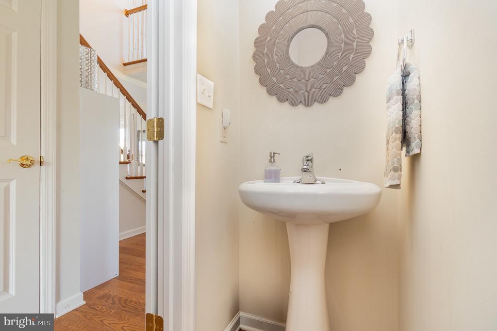 Small bathroom with a white pedestal sink and round decorative mirror beside an open doorway to a staircase.