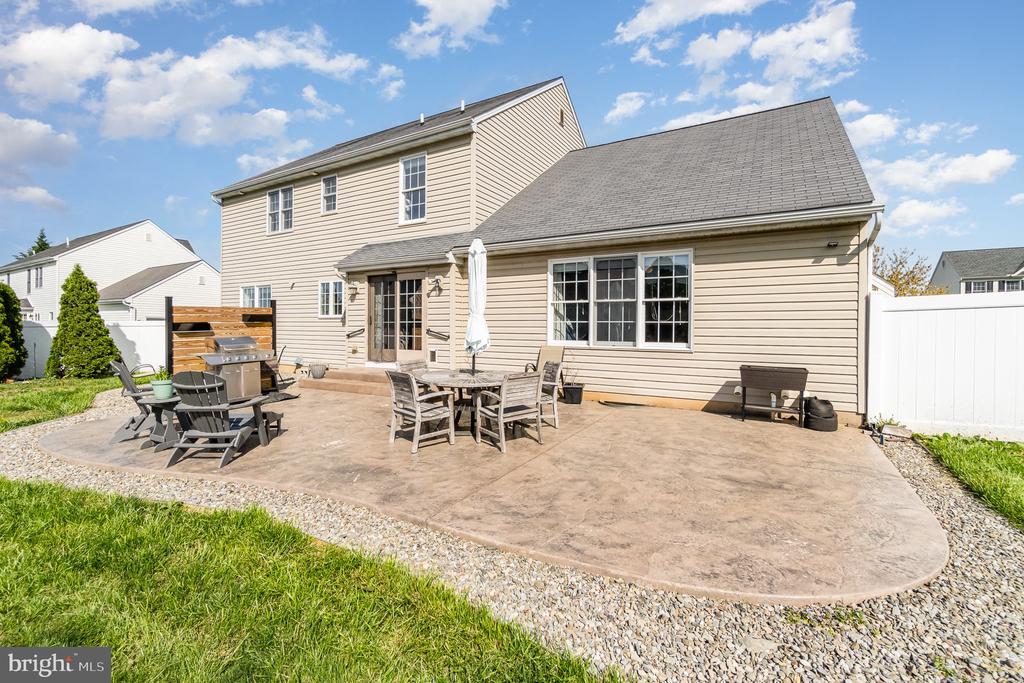 Rear of a beige two-story home with a spacious paved patio, outdoor dining furniture, and grill.