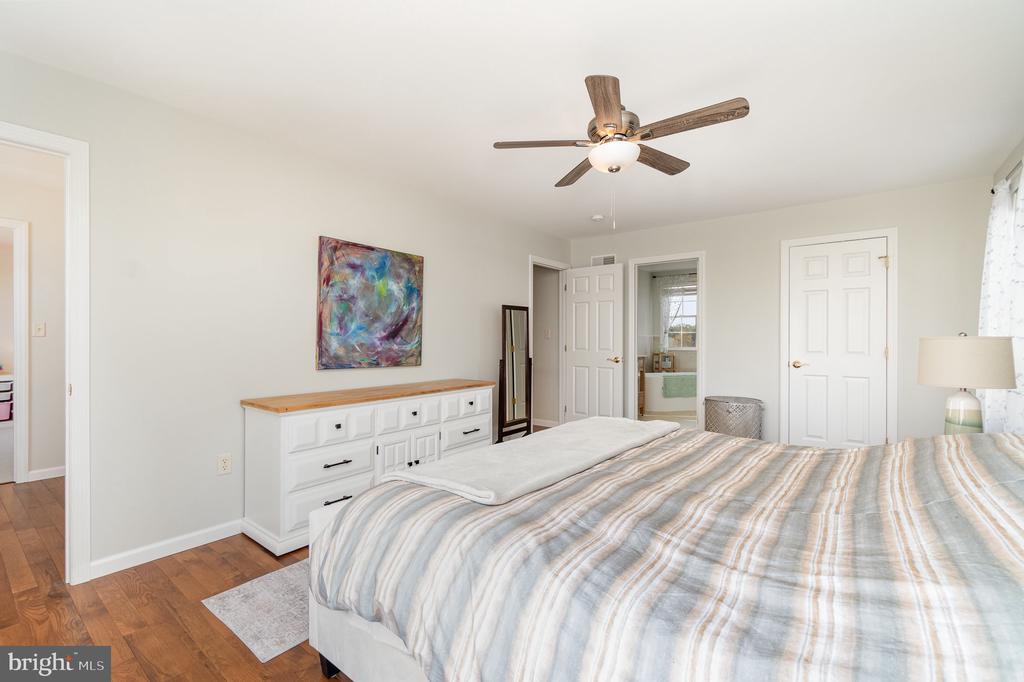 Bedroom with a striped bedspread, white dresser, colorful abstract art, and wood ceiling fan.
