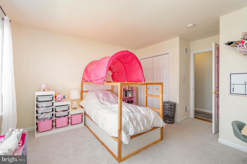 Bedroom with a white bed beneath a pink canopy and colorful storage bins.