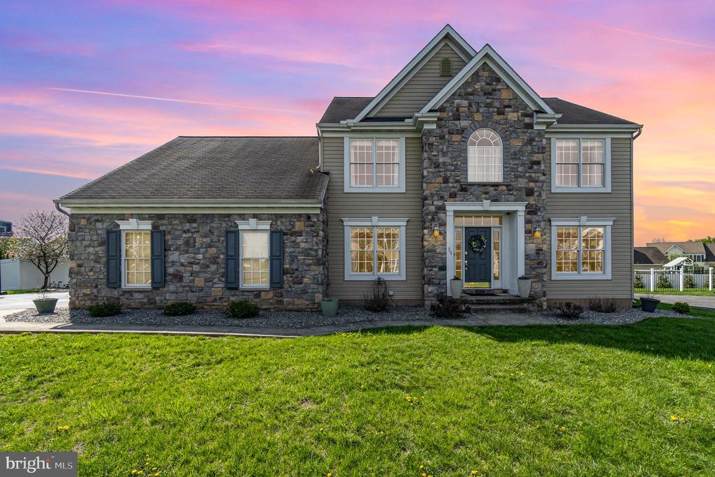 Two-story stone-and-gray-sided house with a green lawn beneath a pink dusk sky.