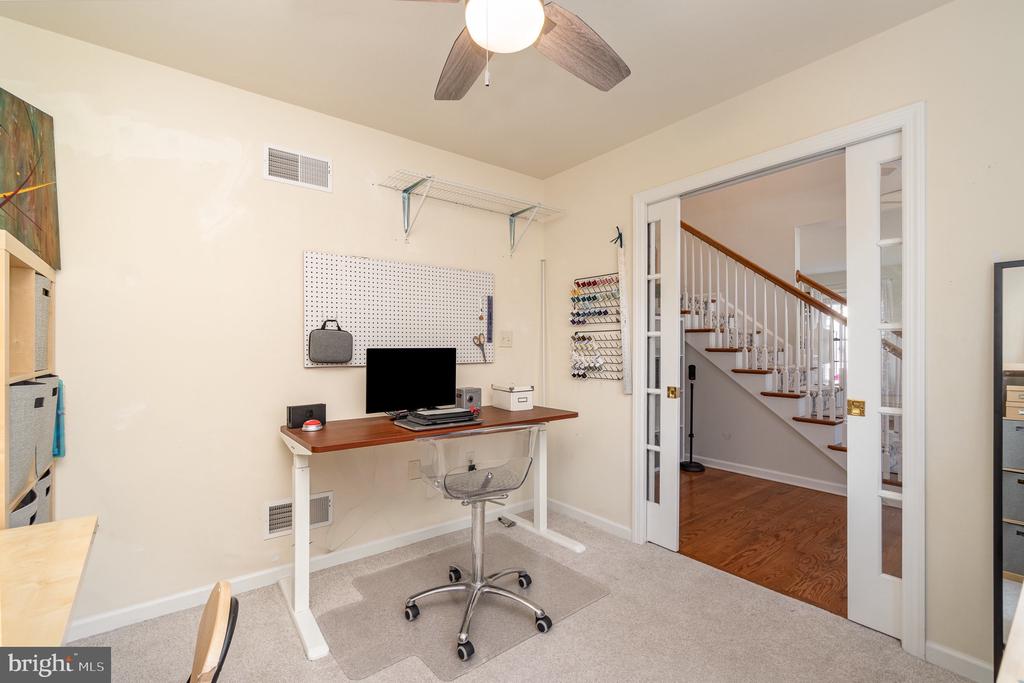Home office with a desk and computer beside open French doors overlooking a wood-trimmed staircase.