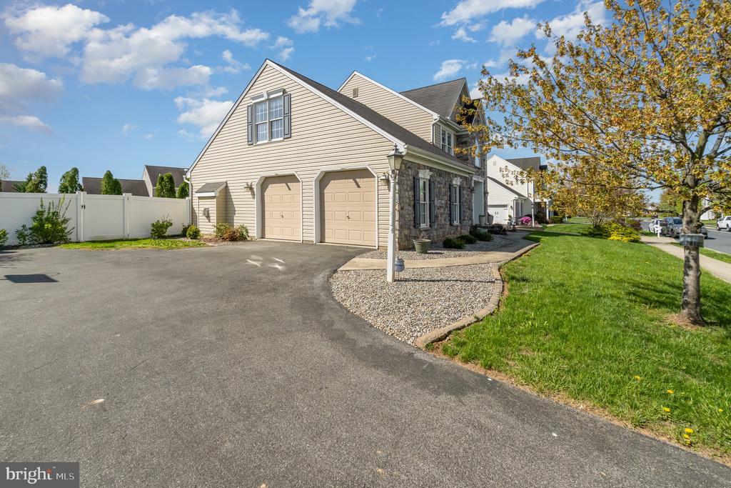 Home exterior with two garage doors, stone accents, a broad driveway, and a white fence.