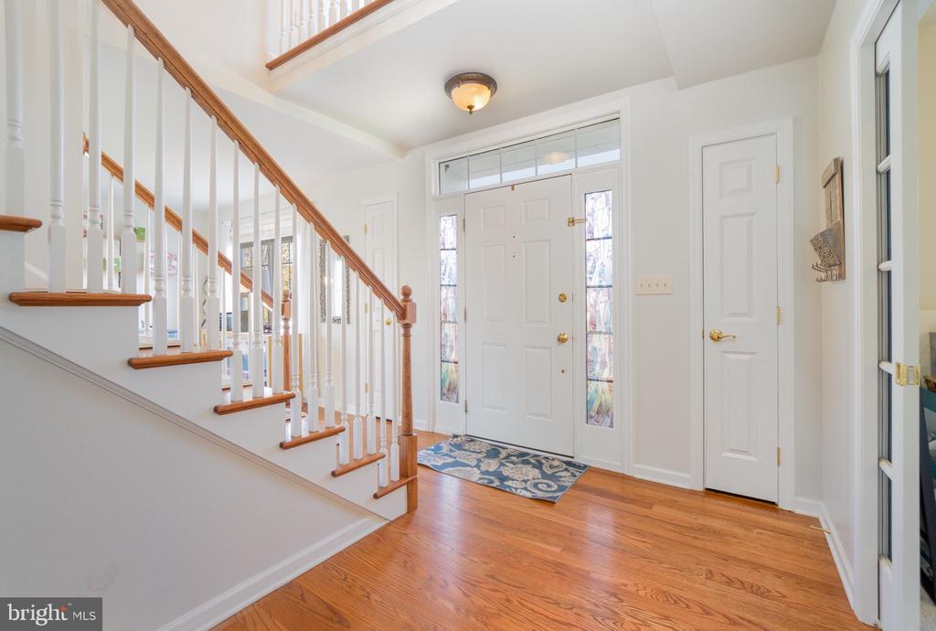 Entry foyer with hardwood floors, a white front door, and a staircase with wood handrails.