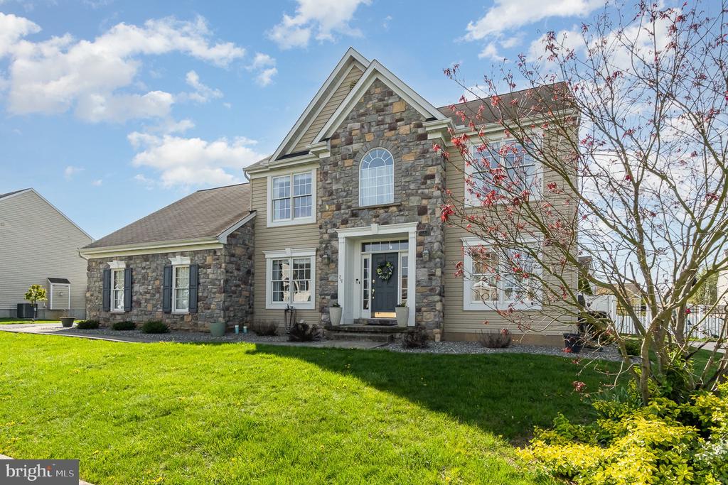 Two-story house with a stone facade, arched window, dark shutters, and a green front lawn.