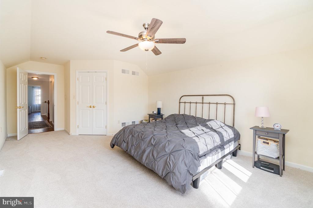 Bedroom with a metal-frame bed, gray bedding, ceiling fan, and sunlit carpet.