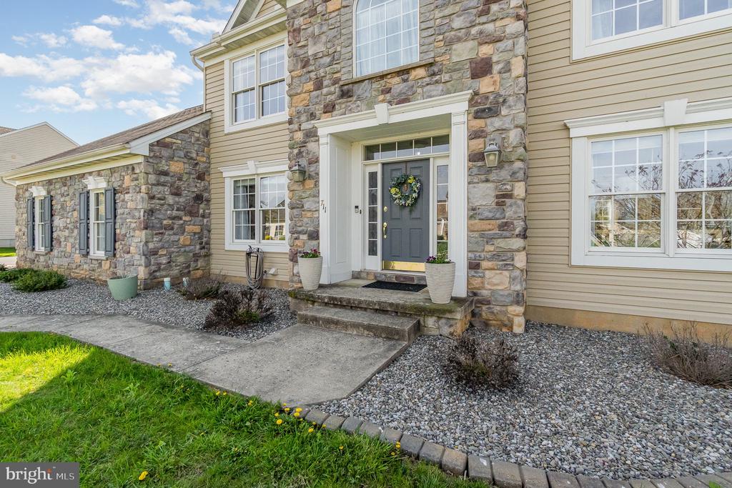 Two-story stone-and-siding home with a gray front door, wreath, and landscaped entrance.