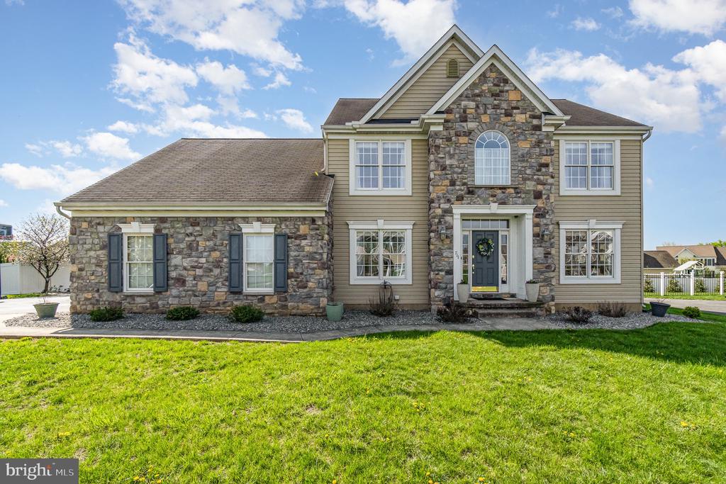 Two-story home with stone facade, central arched window, and broad green front lawn.