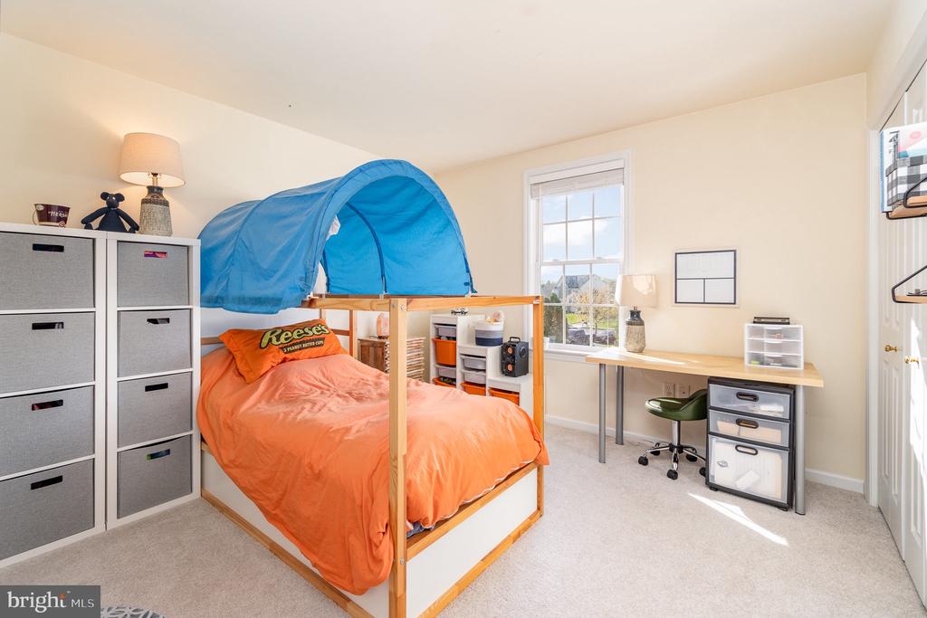 Bedroom with an orange-covered bed beneath a blue tent canopy and a desk beside the window.