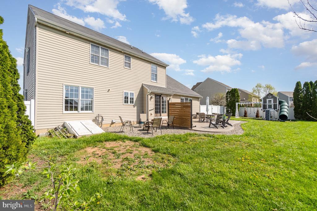 Rear of a beige two-story home with a gravel patio, outdoor furniture, and a backyard playset.