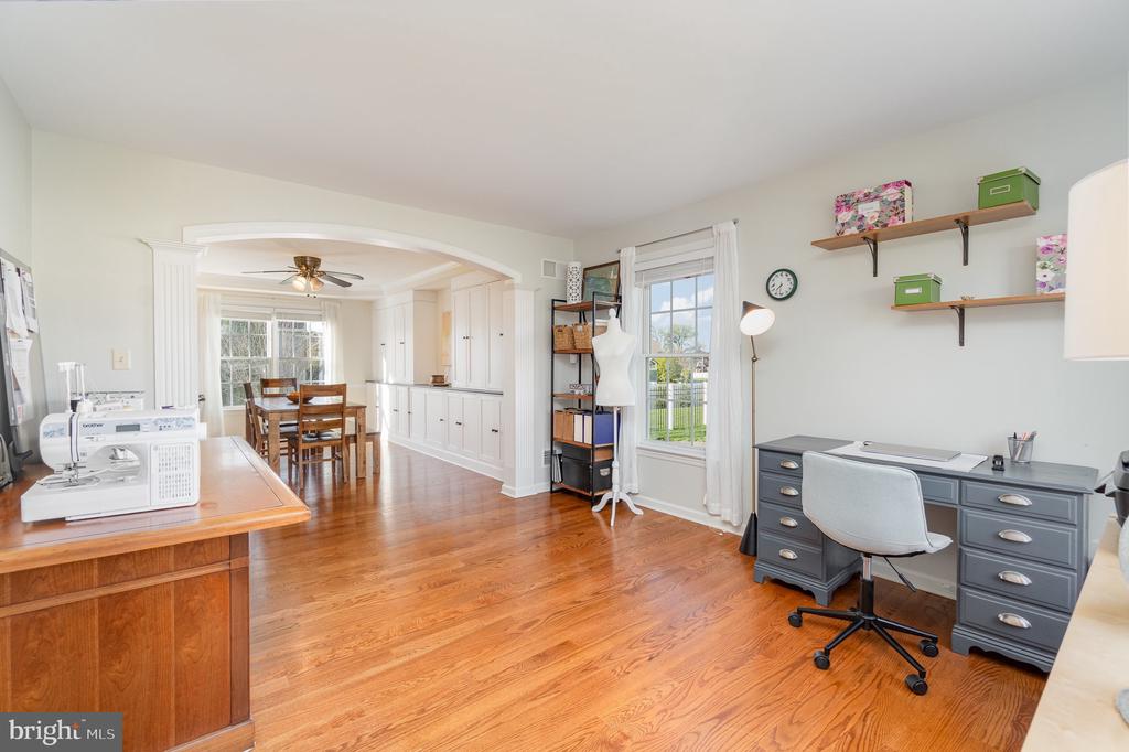 Home office and craft room with a sewing machine, gray desk, hardwood floors, and an arched opening to the dining area.