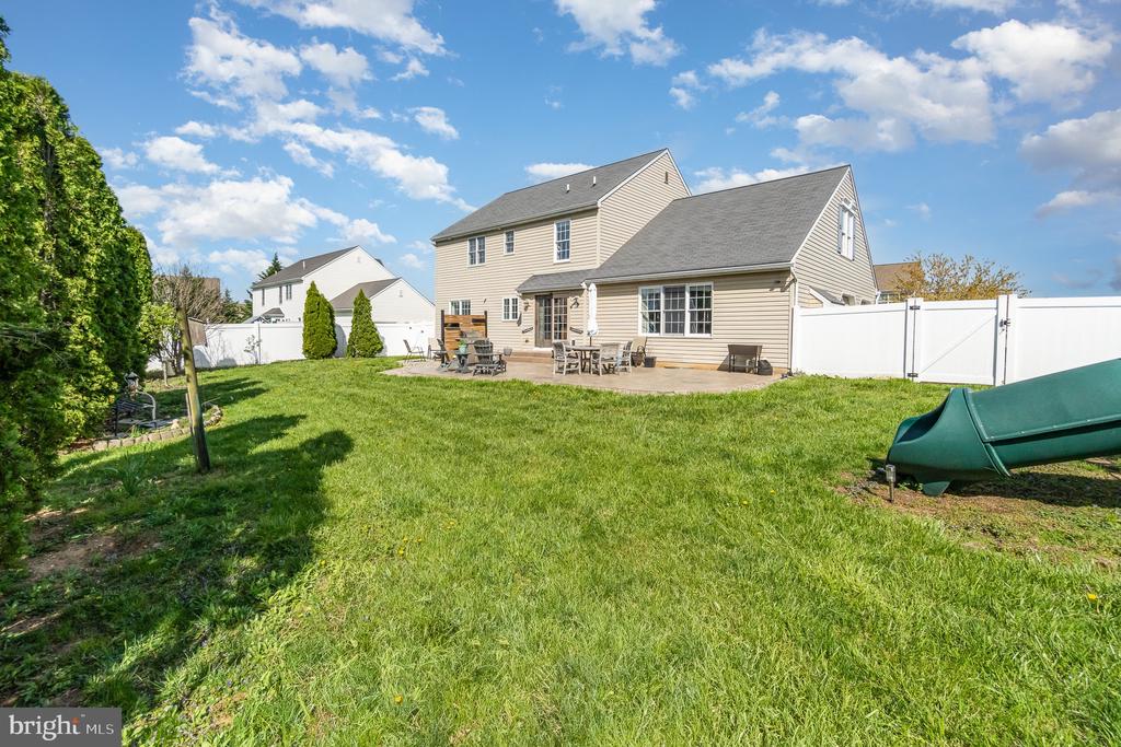 Two-story beige home behind a broad lawn, with a fenced patio and green slide.