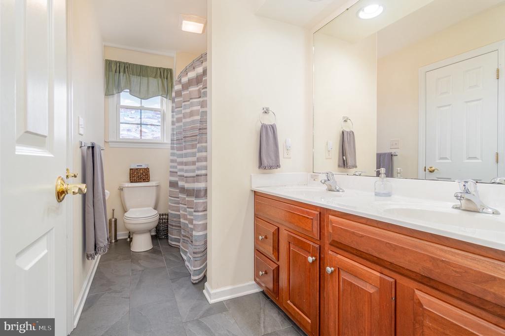 Bathroom with a double-sink wood vanity, gray tile floor, and curtained shower.