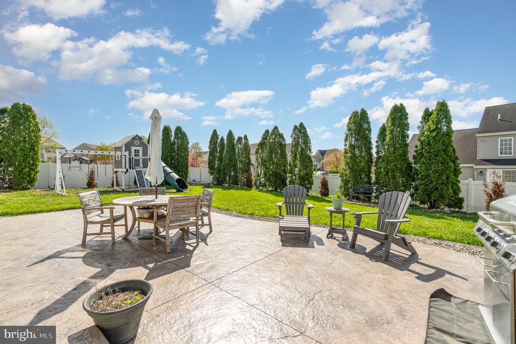Backyard patio with stamped concrete, outdoor dining furniture, lounge chairs, and a playset beyond the lawn.