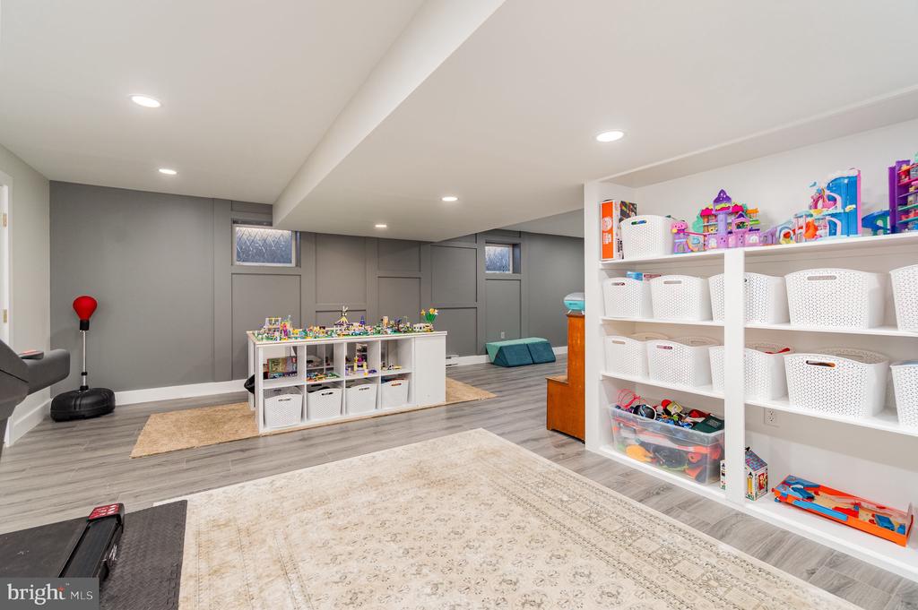 Finished playroom with toy-filled white shelves, gray paneled walls, and a low central cubby unit.