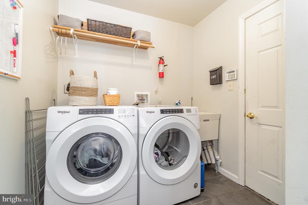 Laundry room with two front-loading washers, a utility sink, and a shelf with baskets.