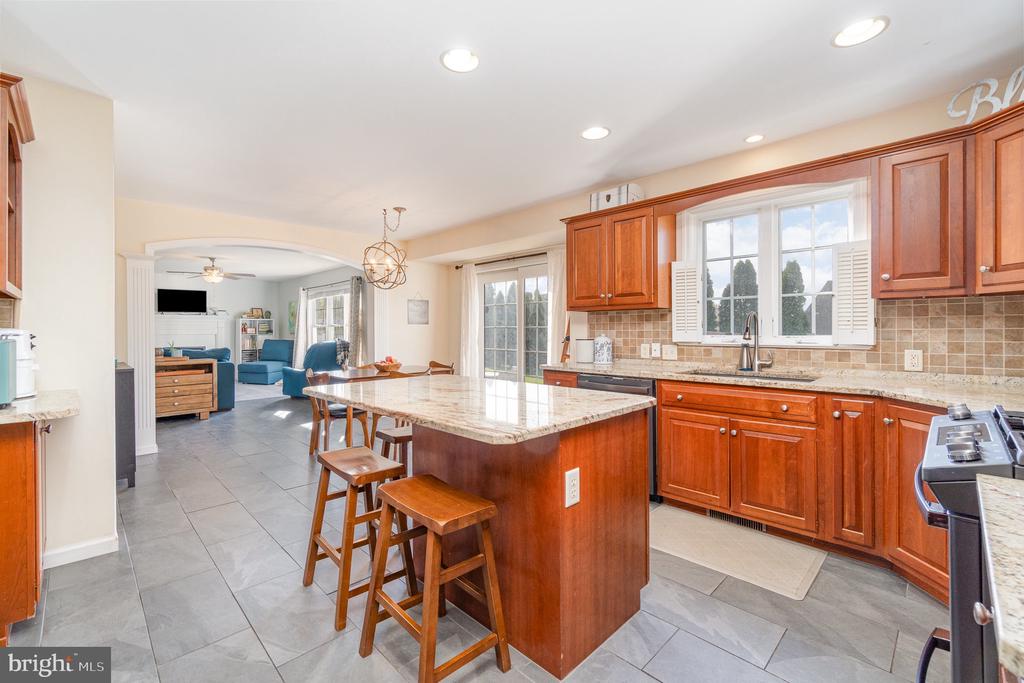 Kitchen with reddish wood cabinets, a granite island, bar stools, and an open archway to the living room.